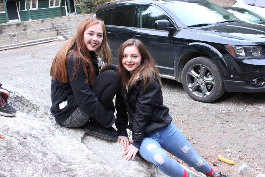 Two smiling girls sitting on a rock outdoors during a sunny nature trip.